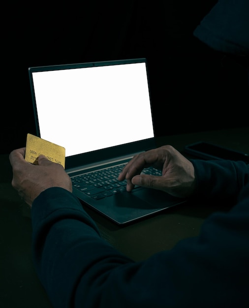 A close-up of a hand trying to steal a credit card through a laptop screen, symbolizing online fraud and identity theft. The background is dark and blurry to emphasize the concept of digital crime.
