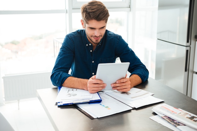 A young professional sitting at a desk, using a financial planning app on their tablet with a positive and focused expression. The office environment in the background is clean and modern, suggesting efficiency and technological integration.