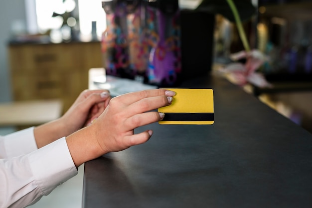 A close-up shot of a hand reaching for a credit card at a checkout counter, with a blurred background of store shelves. The image conveys the ease and temptation of impulsive spending.