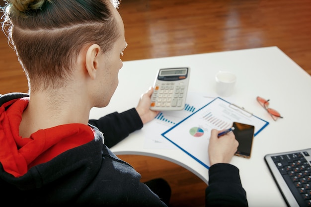 A person using a calculator and laptop to compare debt consolidation options, with charts showing potential savings from different scenarios.