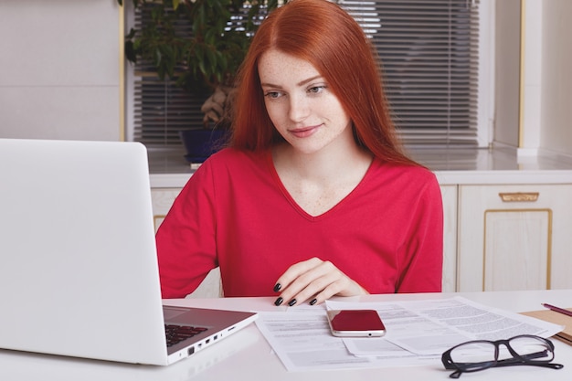 A woman using a laptop while reviewing financial documents at her home office, showcasing proactive financial planning.