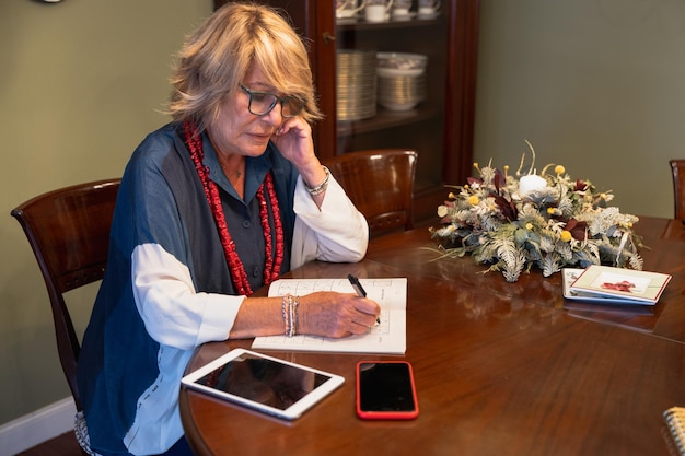 An elderly woman sitting at her kitchen table, reviewing her budget with a calculator and notepad. She has a concerned but determined expression as she analyzes her finances.