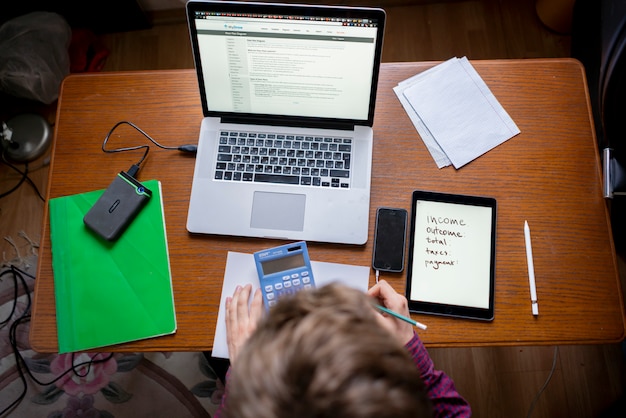A student working on a laptop, filling out the FAFSA form with concentration. The screen displays sections of the application, and the student has a calculator and financial documents nearby.