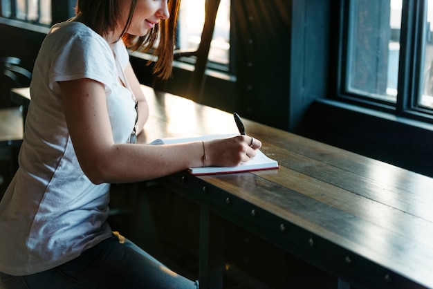 A close-up shot of a student's hand writing in a journal, with a blurred background showing a college campus. The focus is on the act of writing and reflection.