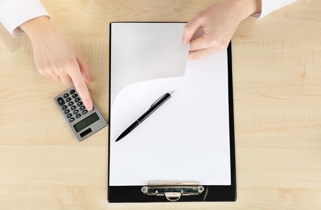 A close-up shot of a hand filling out a FAFSA form on a desk with financial documents and a calculator nearby. The focus is on the act of completing the application.