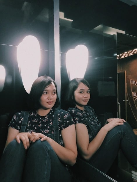 A candid shot of a young K-Drama actor on set, laughing with the crew. He is dressed in casual clothing, and the atmosphere is relaxed and friendly. The background shows various pieces of filming equipment and crew members working.