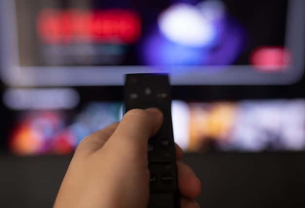 A close-up shot of a person holding a remote control, with various streaming service logos (Netflix, Hulu, HBO Max) subtly glowing on the TV screen in the background.